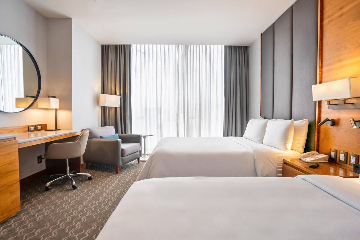 Habitación de hotel con dos camas, un escritorio, una silla, una lámpara, un teléfono y una ventana con cortinas.