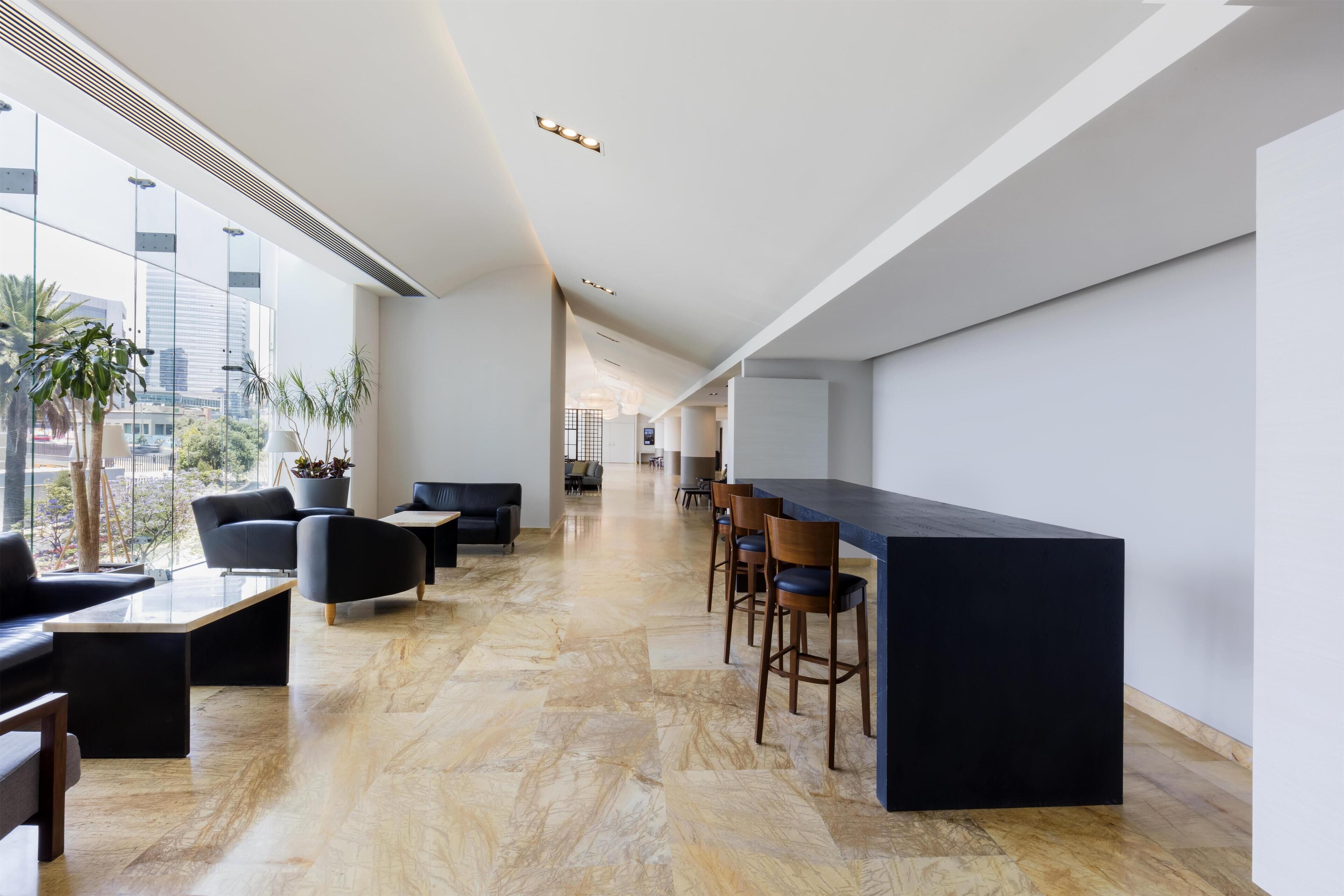 A modern interior with a long bar area, seating, and large windows offering city views.