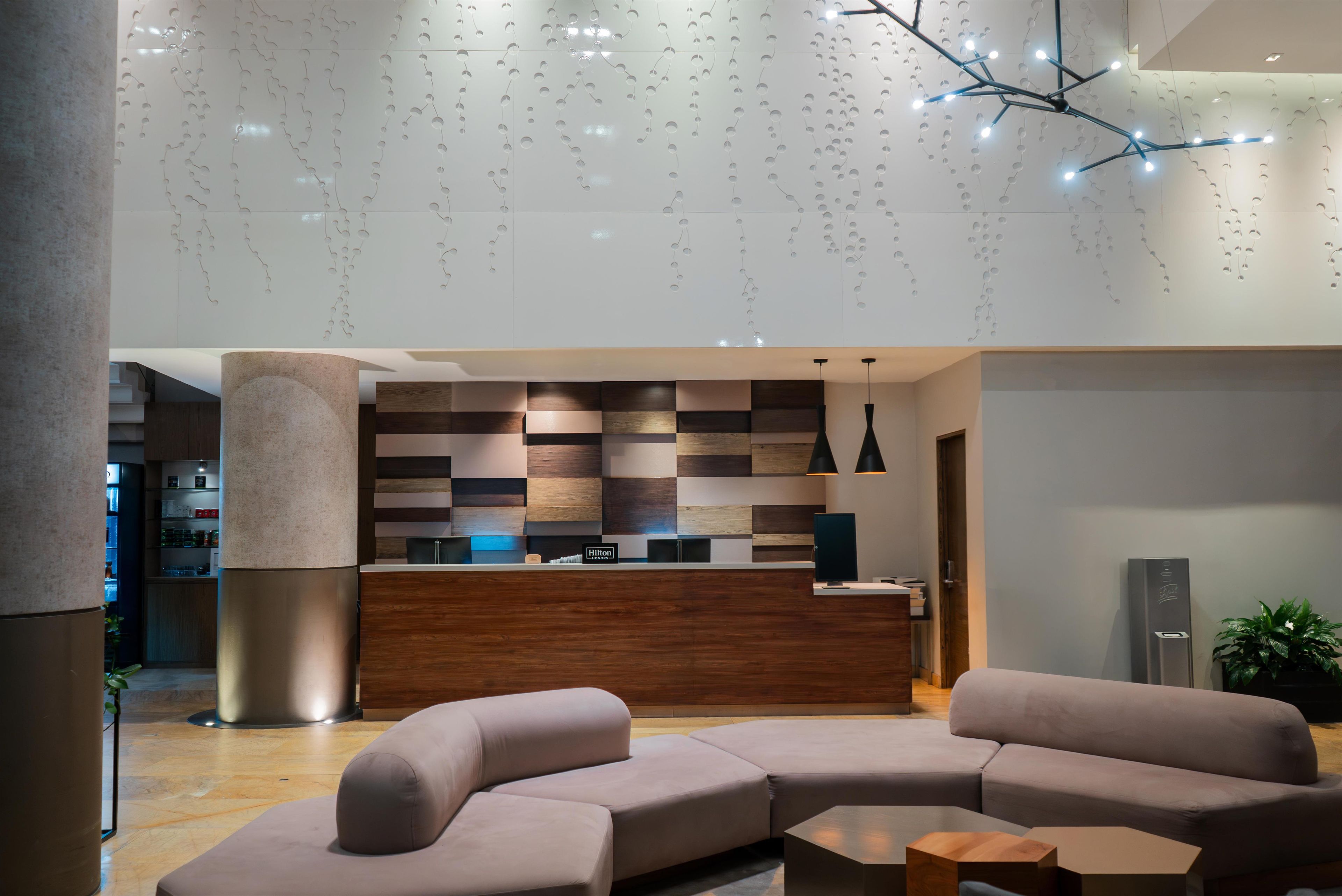En modern hotellobby med en receptionsdisk, soffor och hängande lampor.