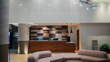 En modern hotellobby med en receptionsdisk, soffor och hängande lampor.