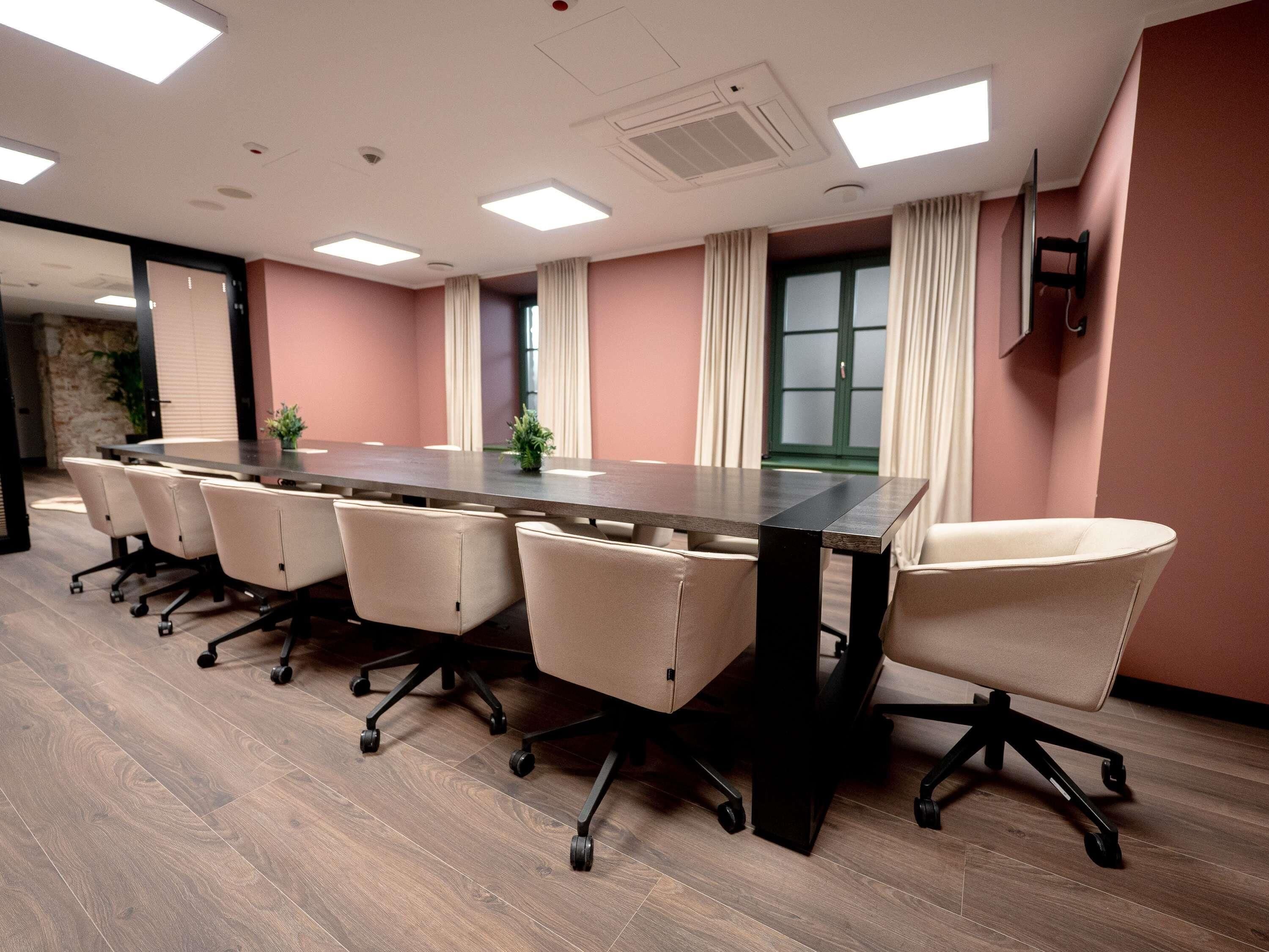 Une salle de conférence avec une longue table, six chaises et une grande fenêtre avec des rideaux.