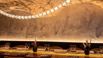 Interior de un restaurante con una larga mesa dispuesta para comer, una pared con el nombre 'Harper Woolf' grabado, y un techo con textura rocosa a la vista.