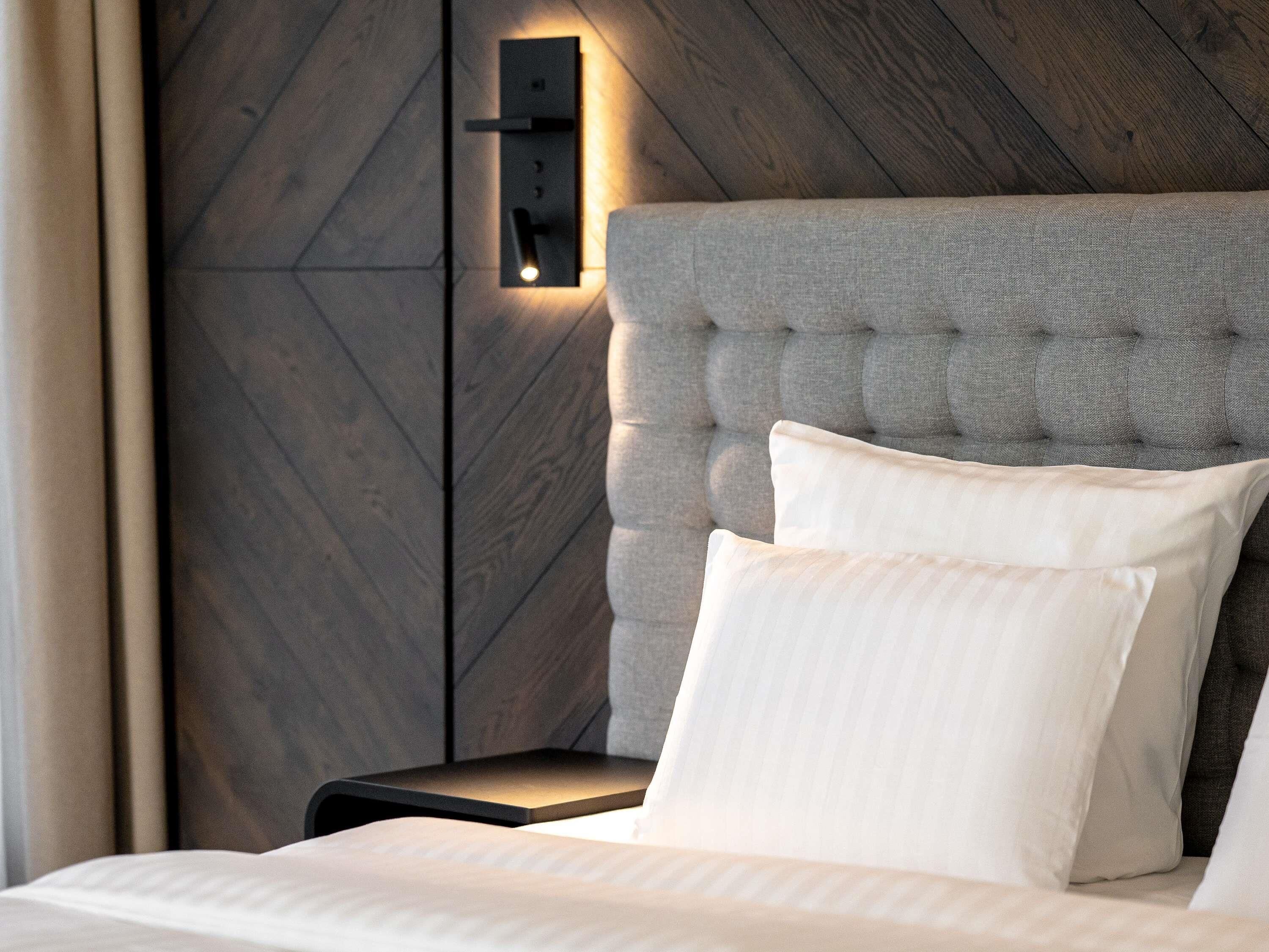 Un dormitorio con cabecera capitonada, una mesita de noche y un aplique de pared.