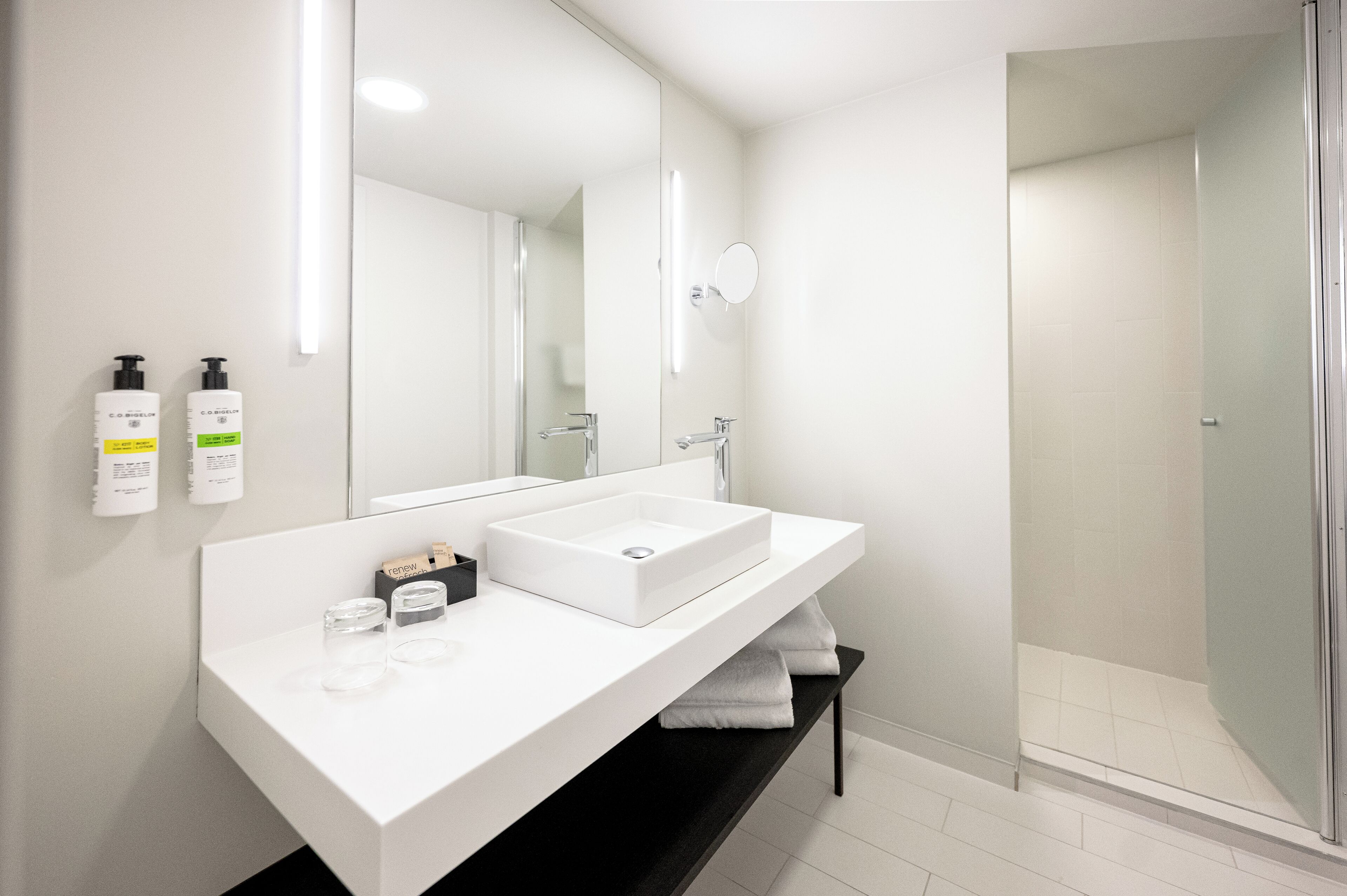A modern bathroom with a white vanity, a large mirror, and a glass-enclosed shower.