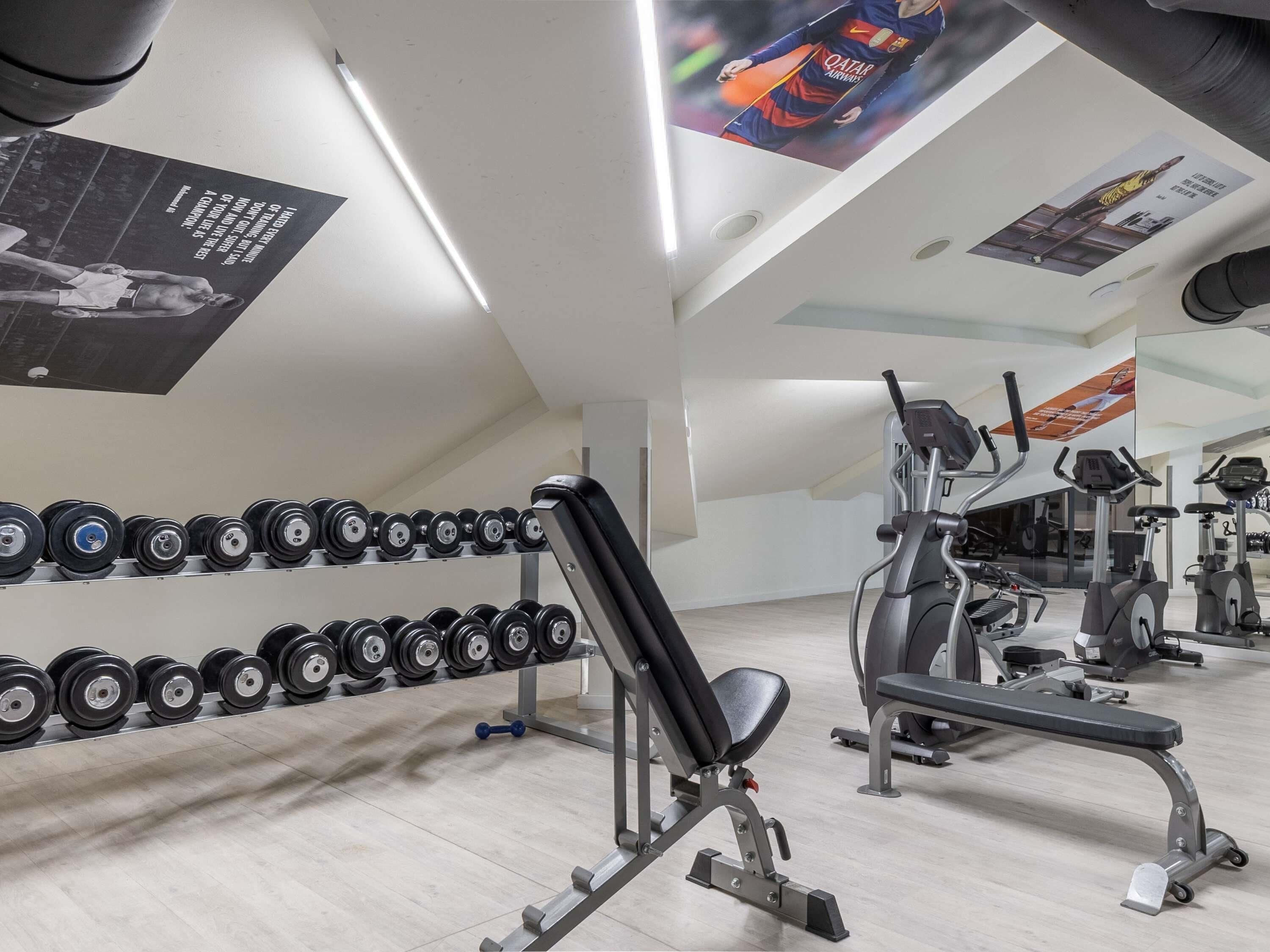 Un gimnasio con equipamiento de ejercicio, estantes para pesas y un espejo grande.