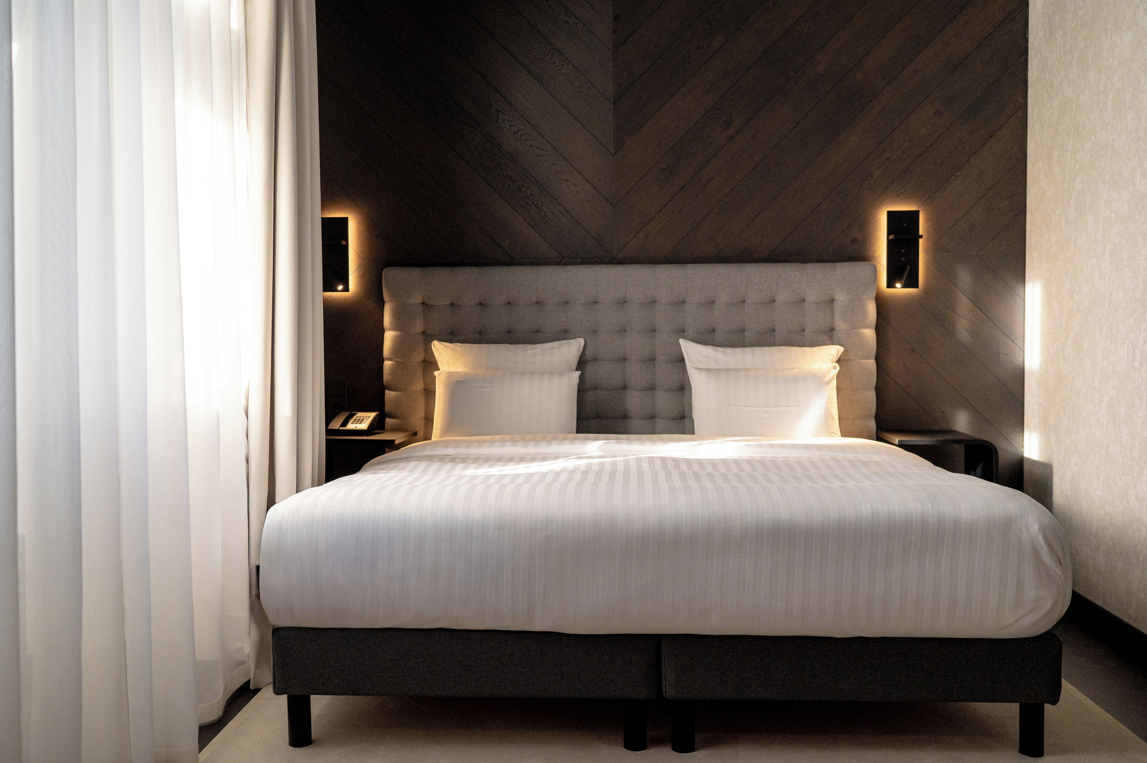 Un dormitorio moderno con una cama grande, un cabecero capitonado y dos lámparas fijadas a la pared.