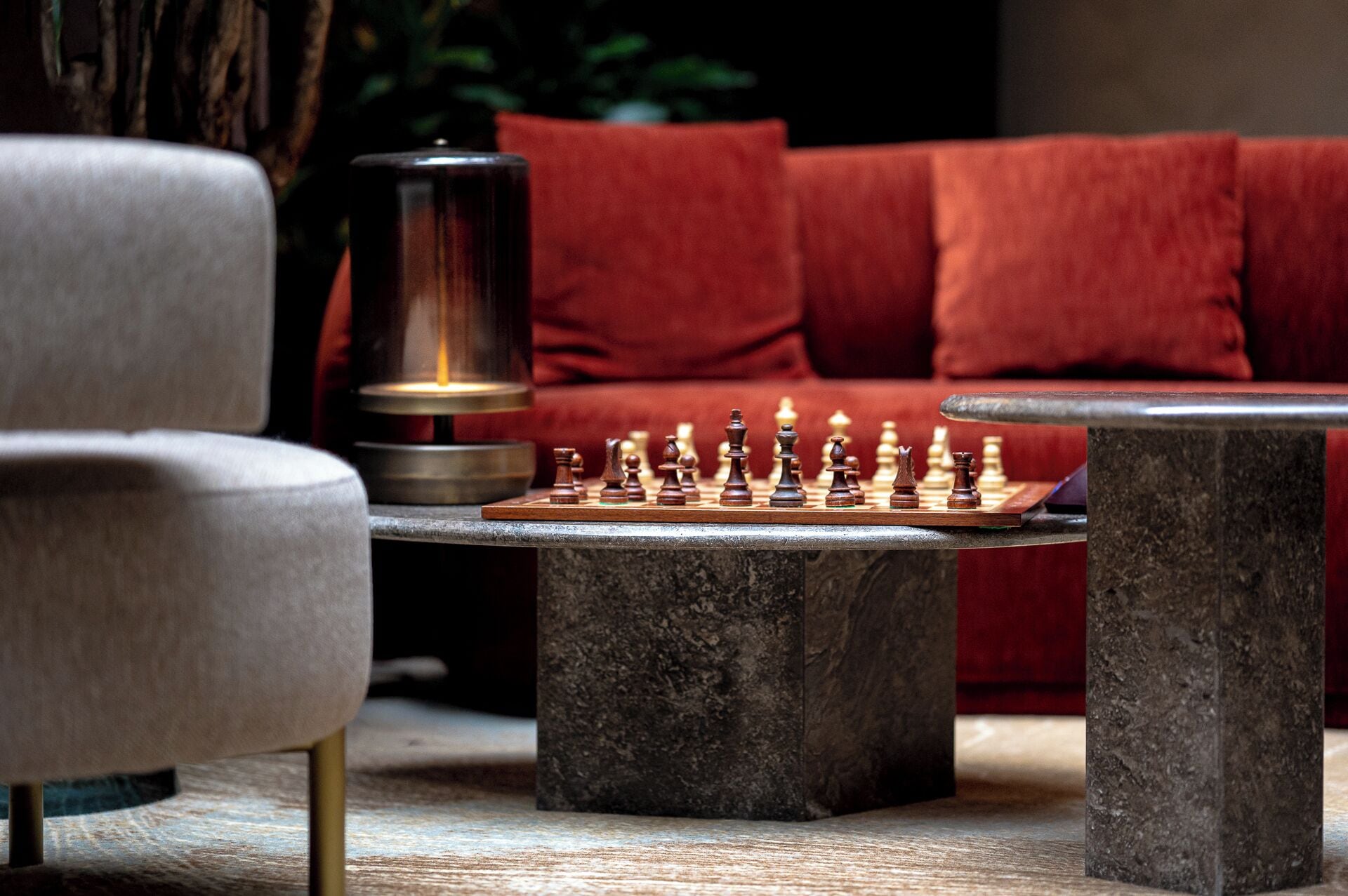 A chessboard on a stone table with a red sofa and a lamp in the background.