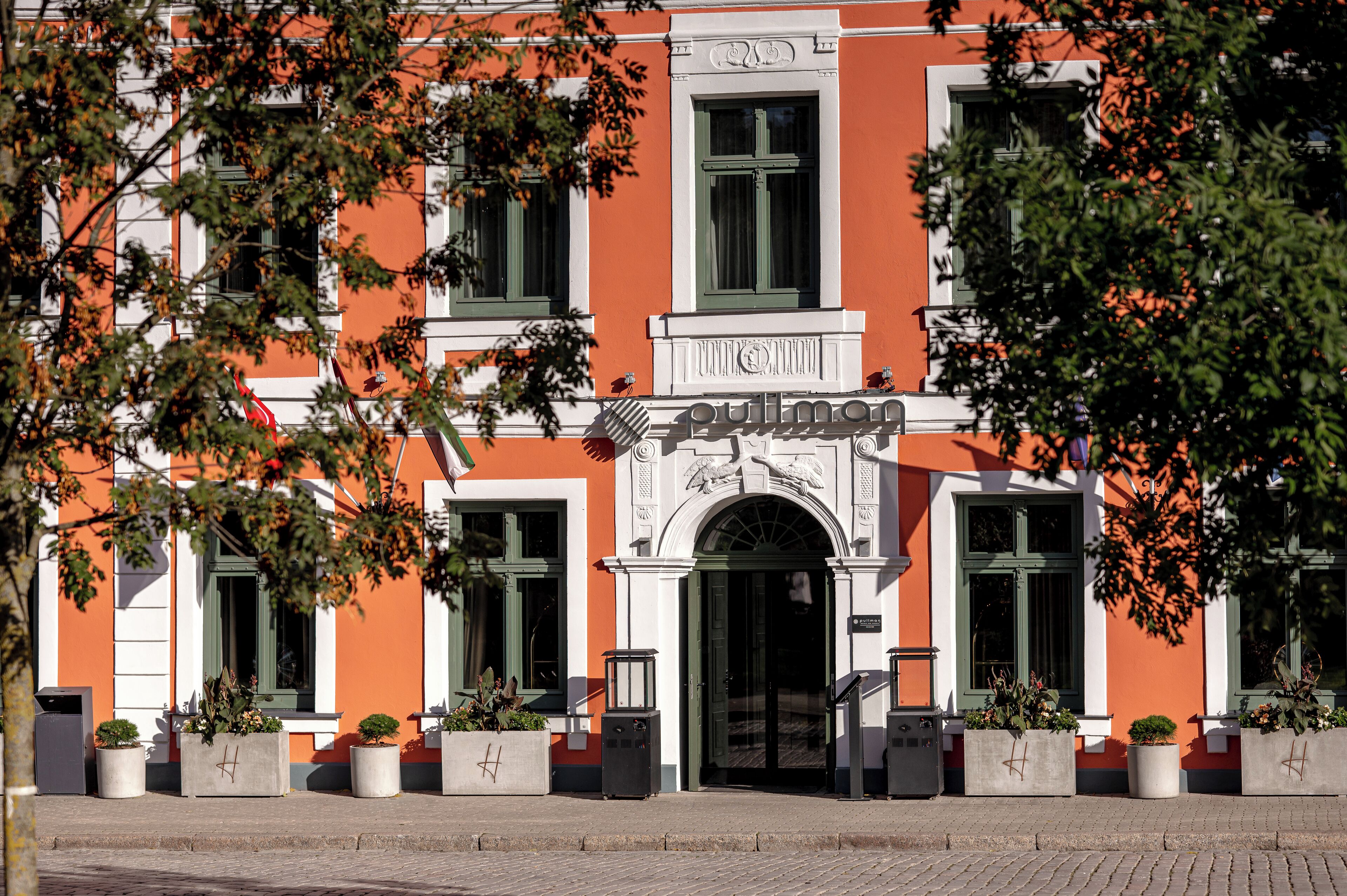 A building with a prominent entrance, a sign above the door, and potted plants in front.