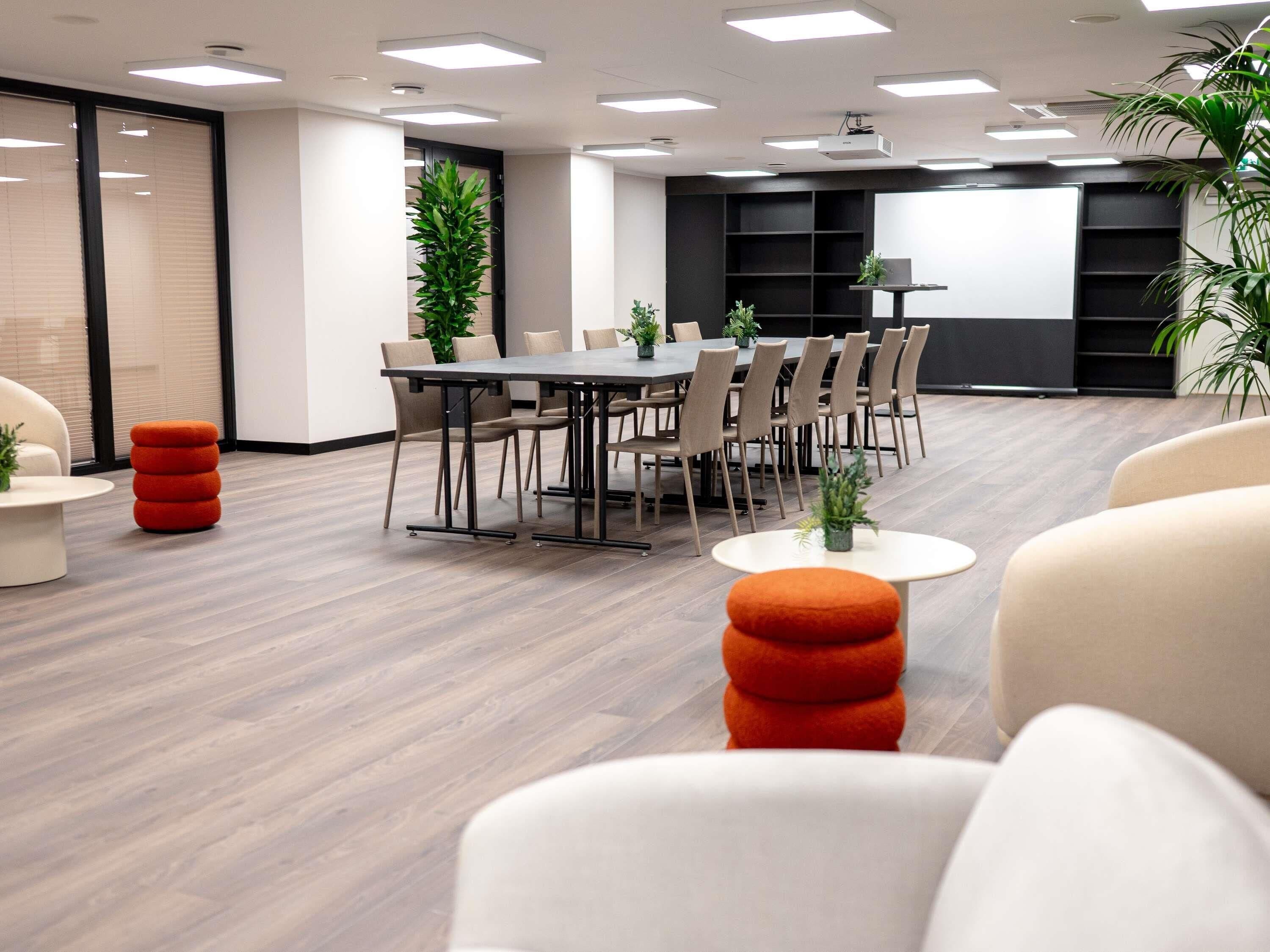 Una sala de reuniones moderna con una mesa larga, sillas y una pantalla para proyector.
