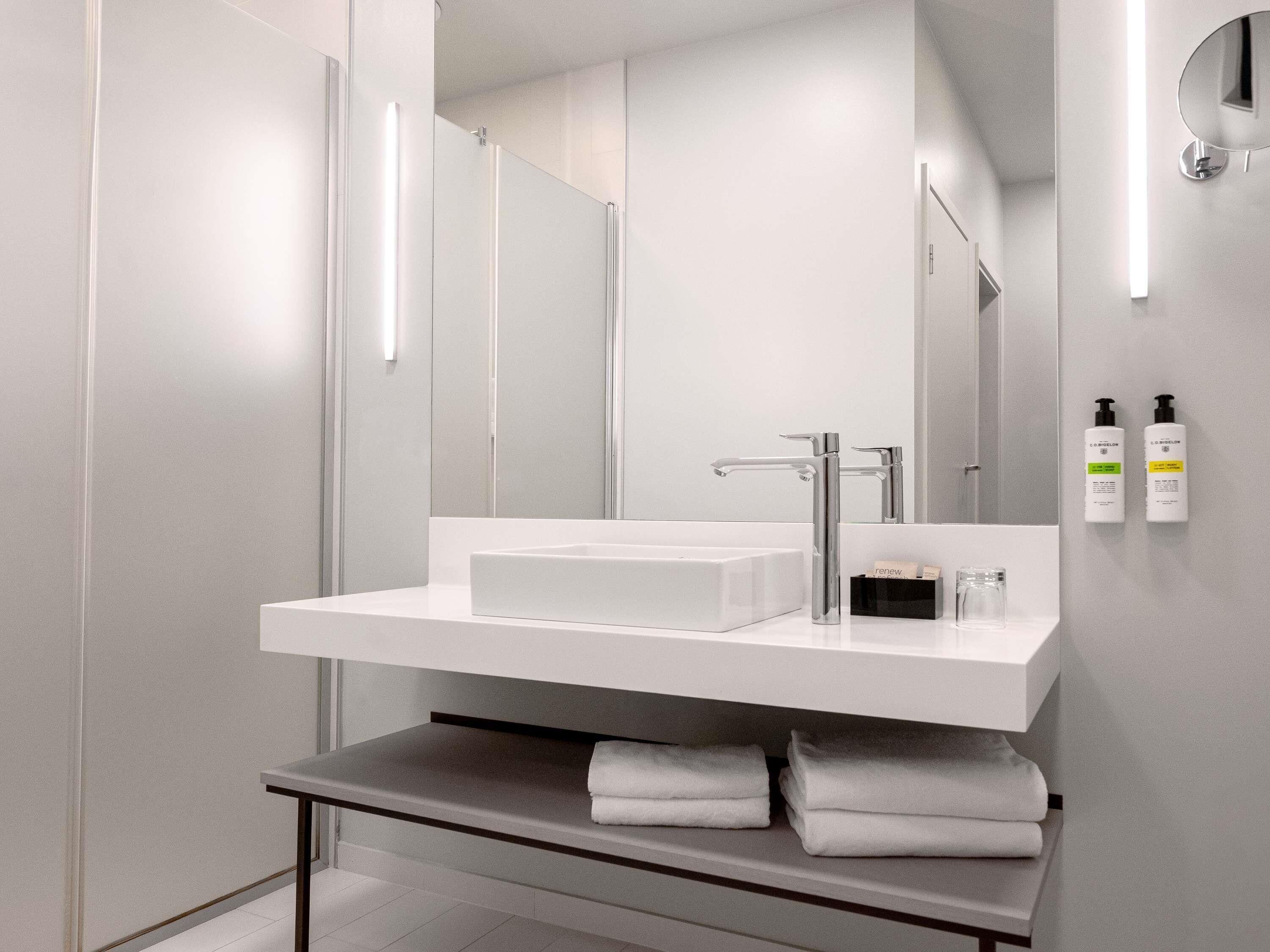 Une salle de bain moderne avec un lavabo blanc, un grand miroir et un porte-serviettes.