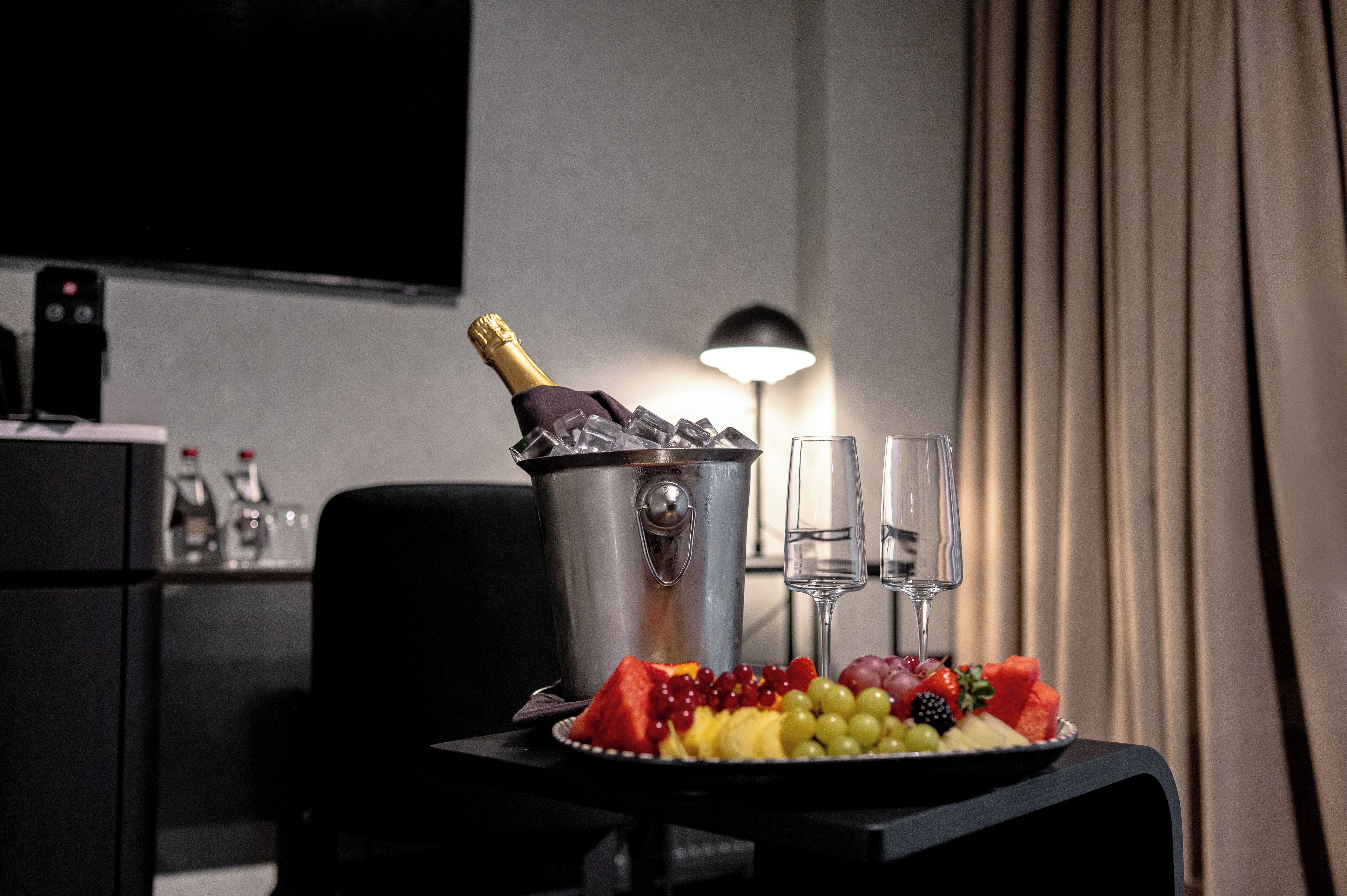 A room with a table set for a meal, including a fruit platter and a bottle of champagne.