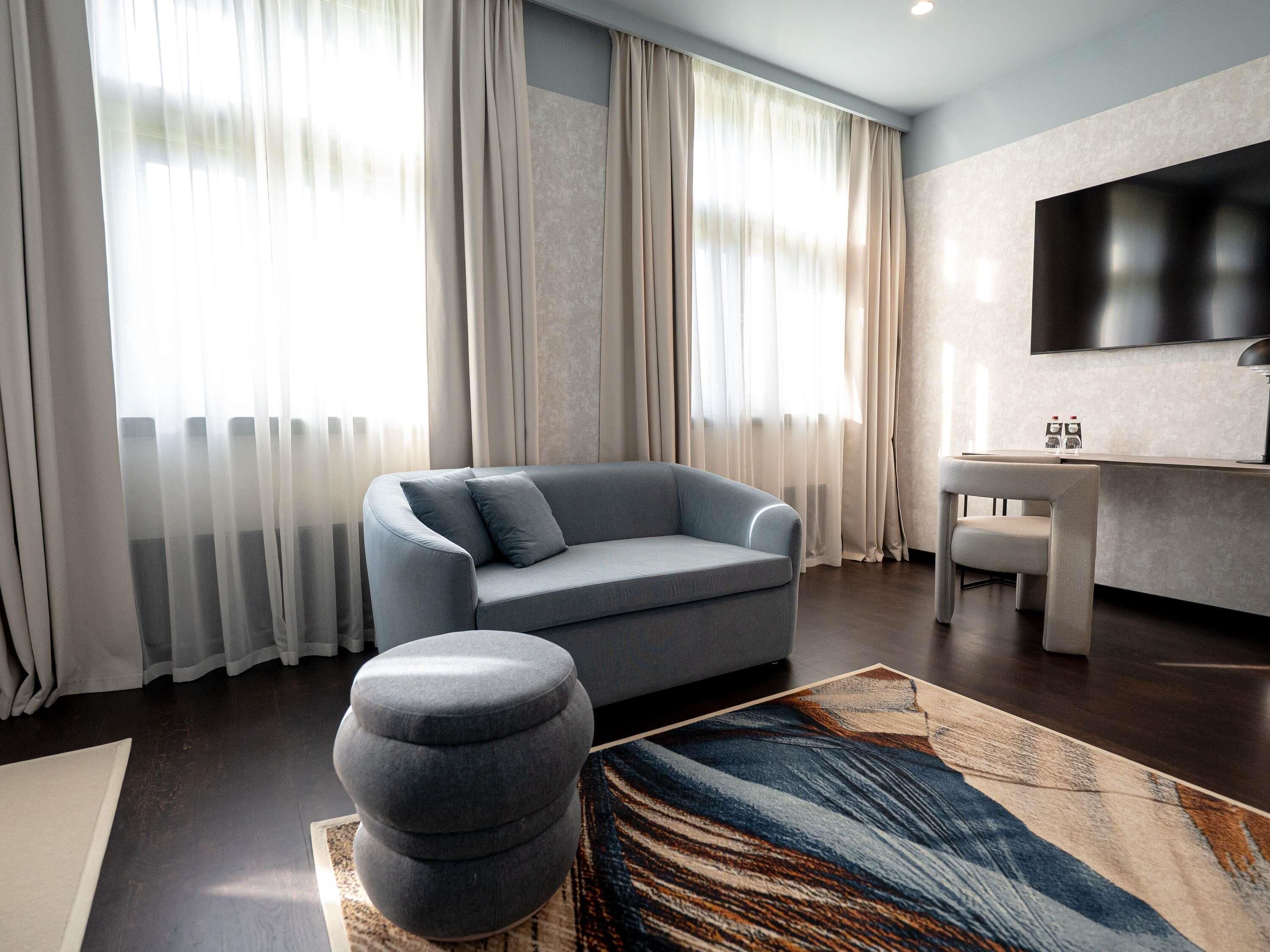 Een moderne woonkamer met een grijze bank, een rond voetenbankje en een groot vloerkleed.