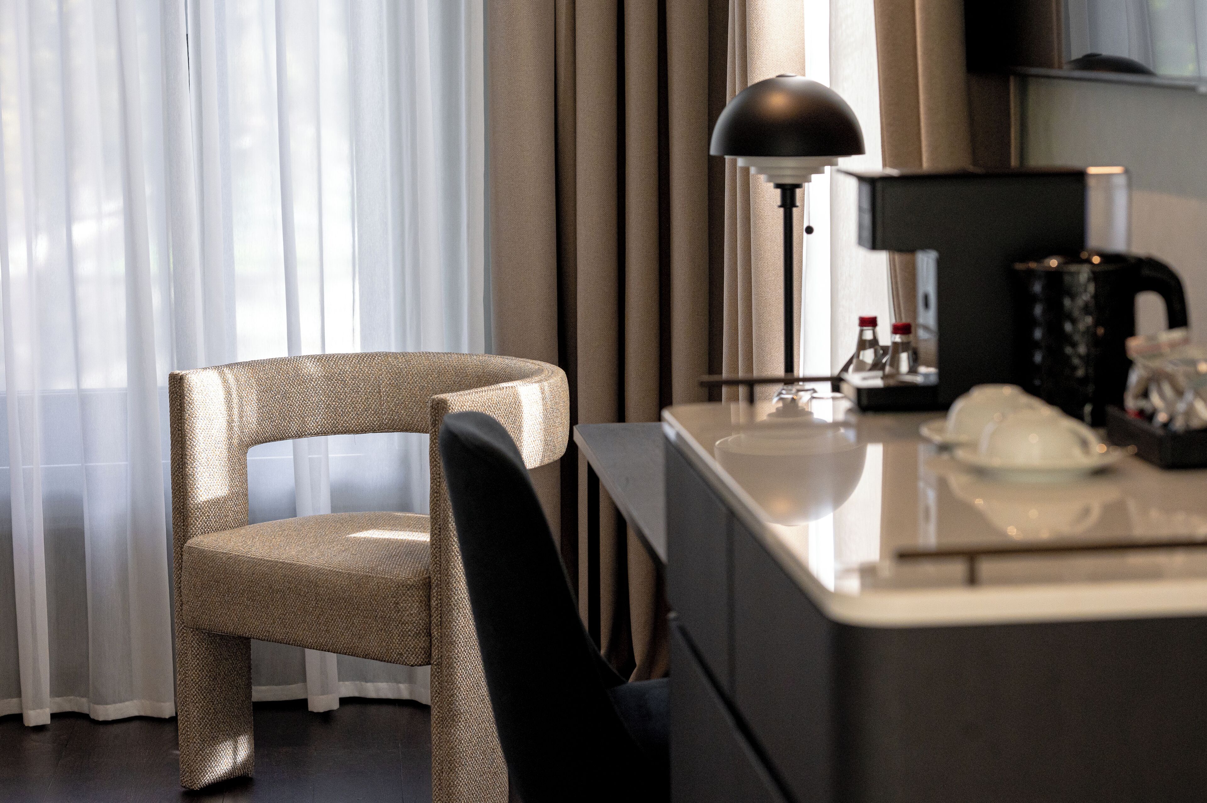 Habitación de hotel con escritorio moderno, una silla, lámpara y cafetera.