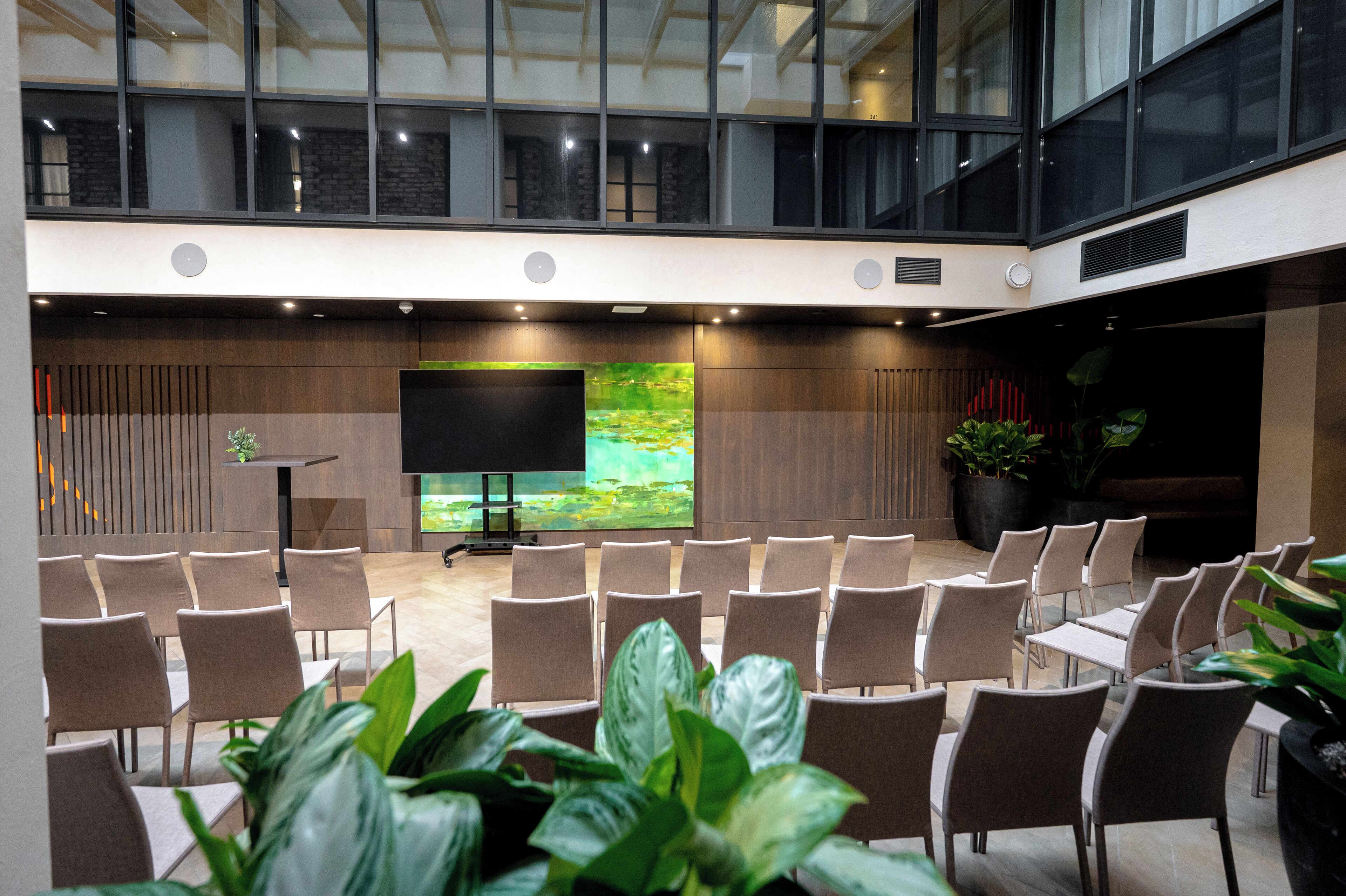 Un salón de conferencias con filas de sillas, una pantalla grande y plantas en macetas.