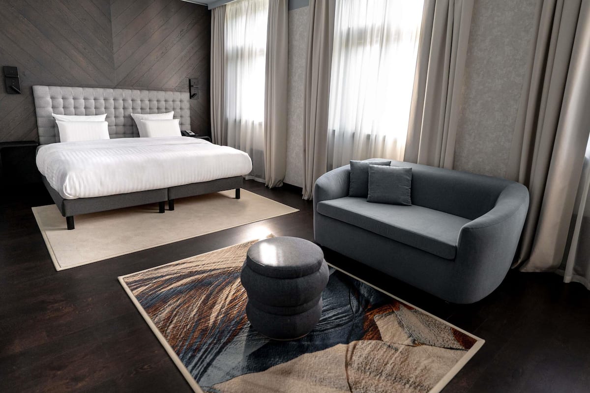 Ein modernes Schlafzimmer mit einem großen Bett, einem grauen Sofa und einem gemusterten Teppich.