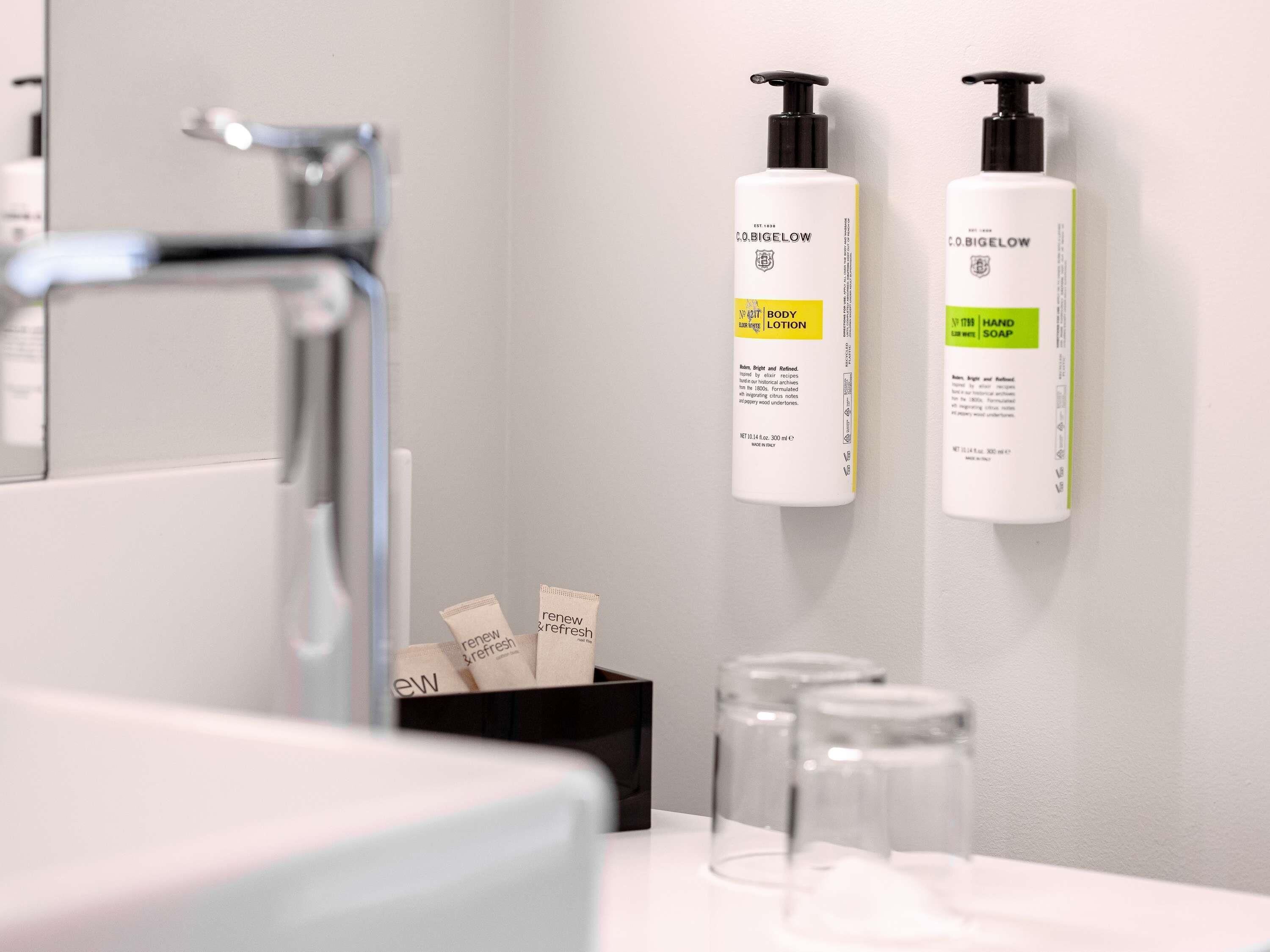 A bathroom with a modern faucet, two bottles of C.O.BIGELOW body lotion, and two bottles of C.O.BIGELOW hand soap.
