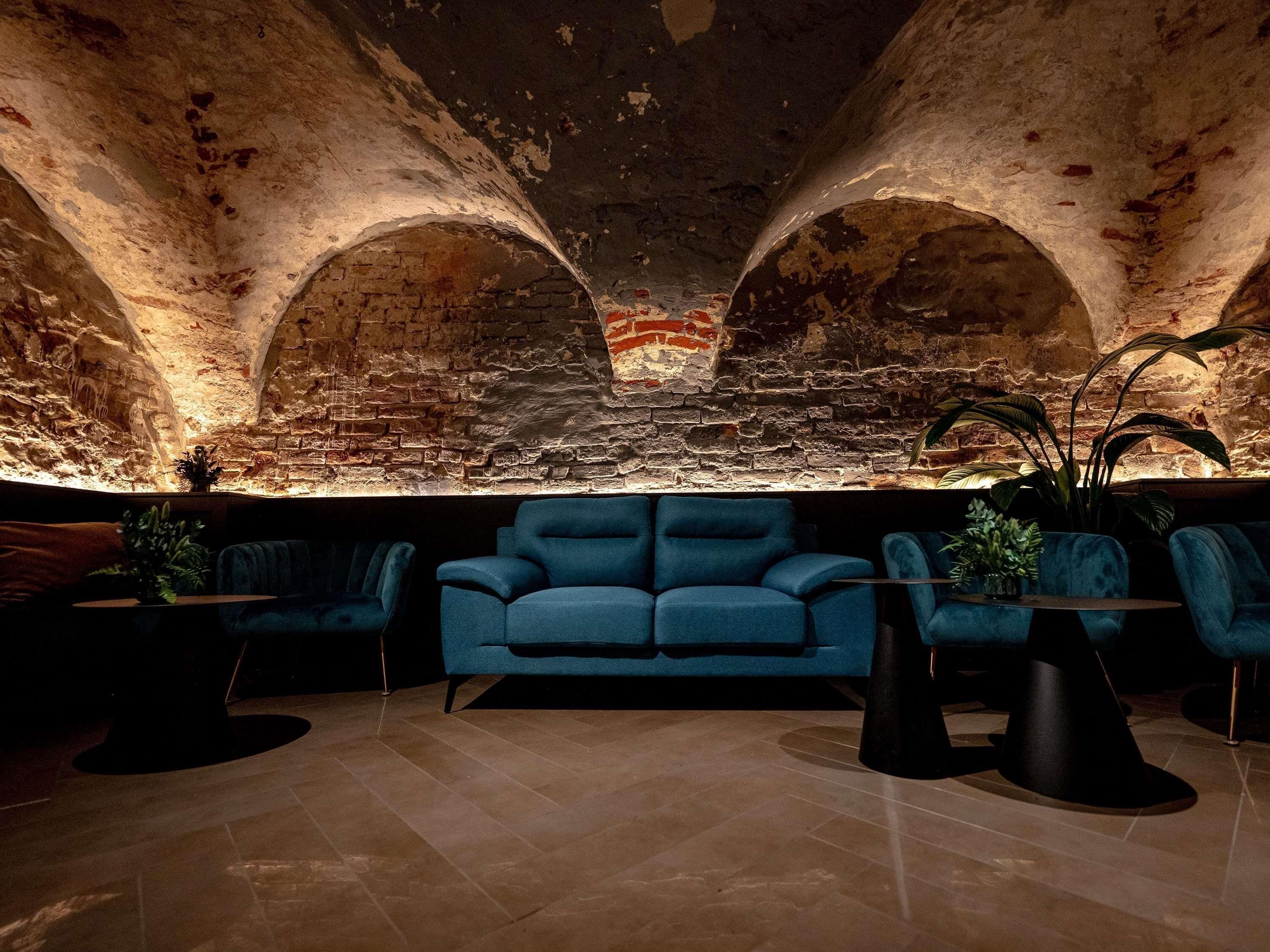 A lobby with a blue sofa, two round tables, and a brick wall with arches.