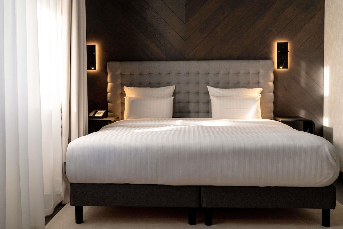 Ein modernes Schlafzimmer mit einer gepolsterten Kopfteil, zwei Nachttischen und einem großen Bett mit weißer Bettwäsche.