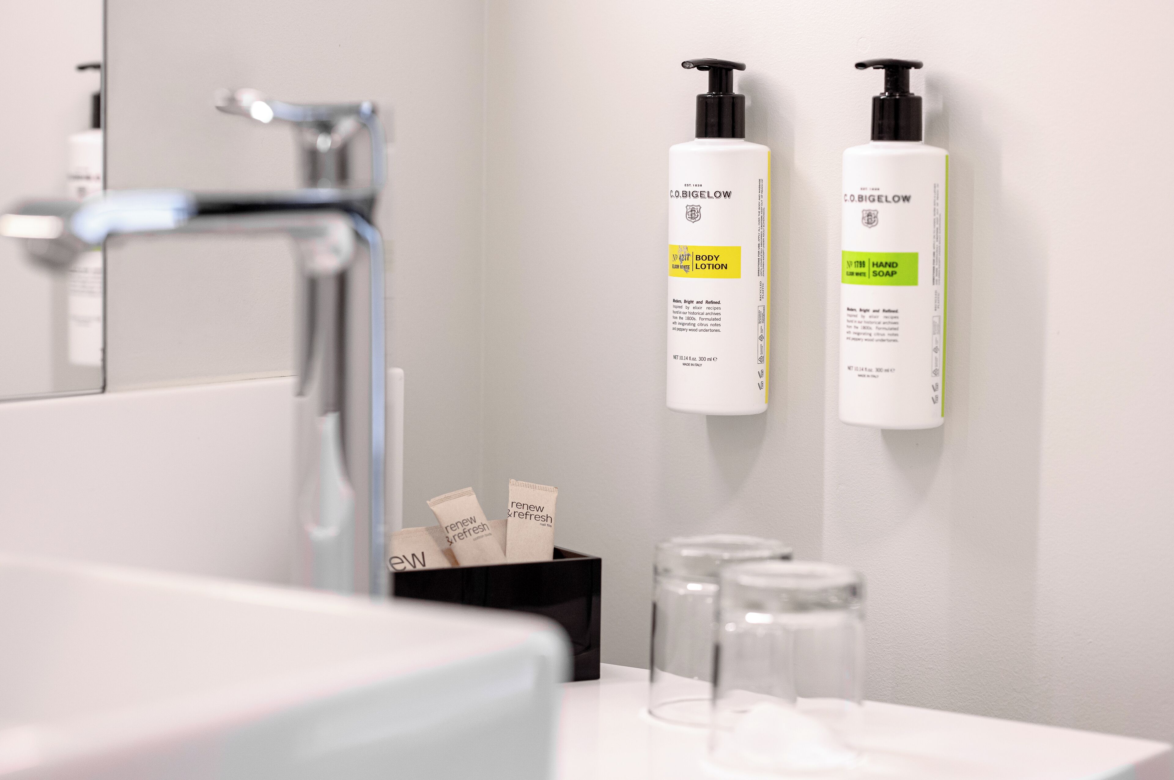 Une salle de bain dotée d’un robinet moderne, de deux flacons de savon liquide et d’un récipient contenant de petits flacons.