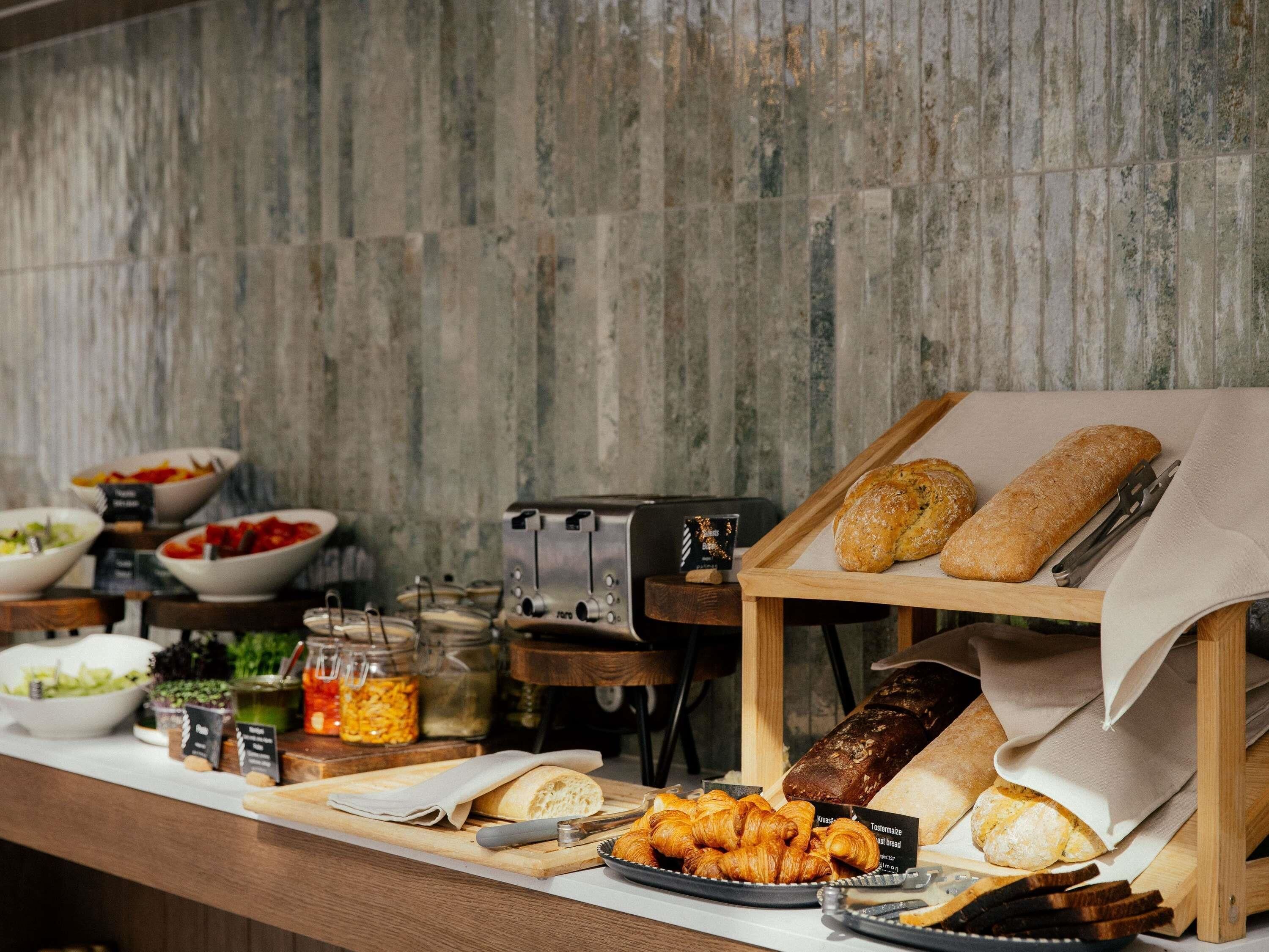 Buffet com diversos pães, bolos e saladas.