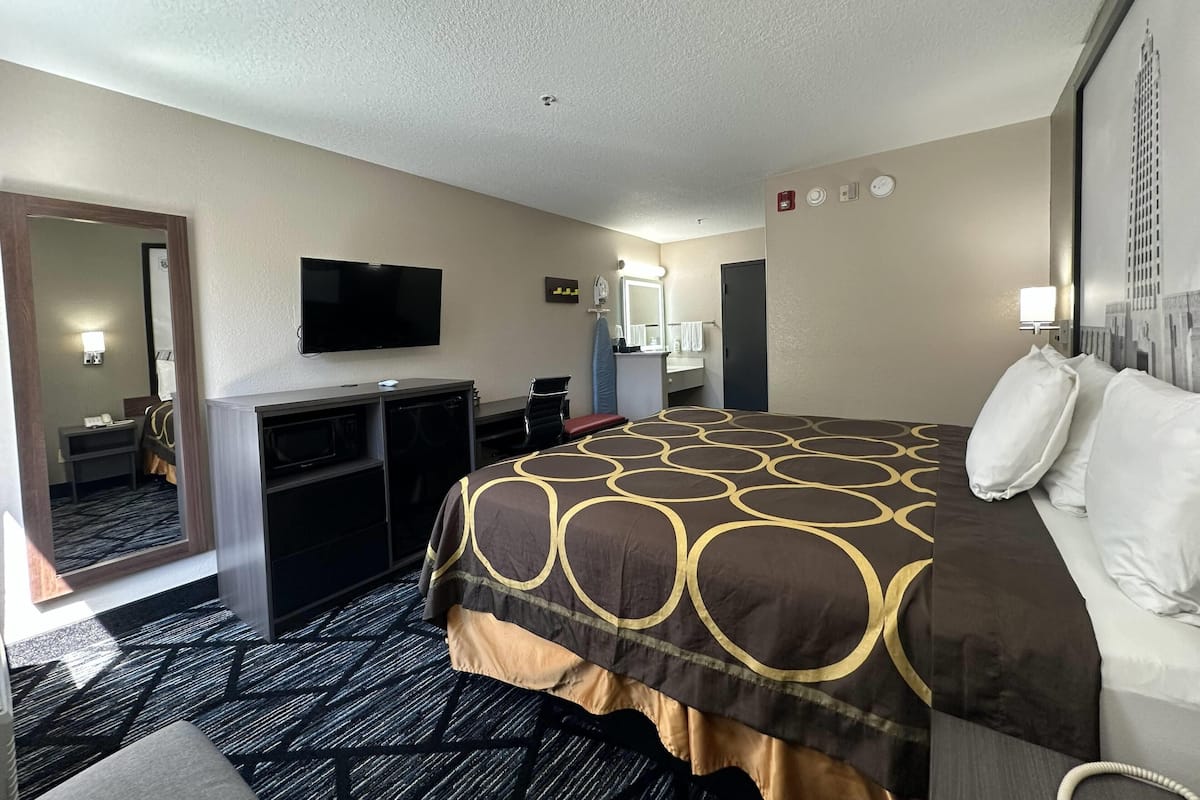 Une chambre d’hôtel avec un lit, un bureau, une télévision, un miroir et une salle de bain visible à travers une porte ouverte.