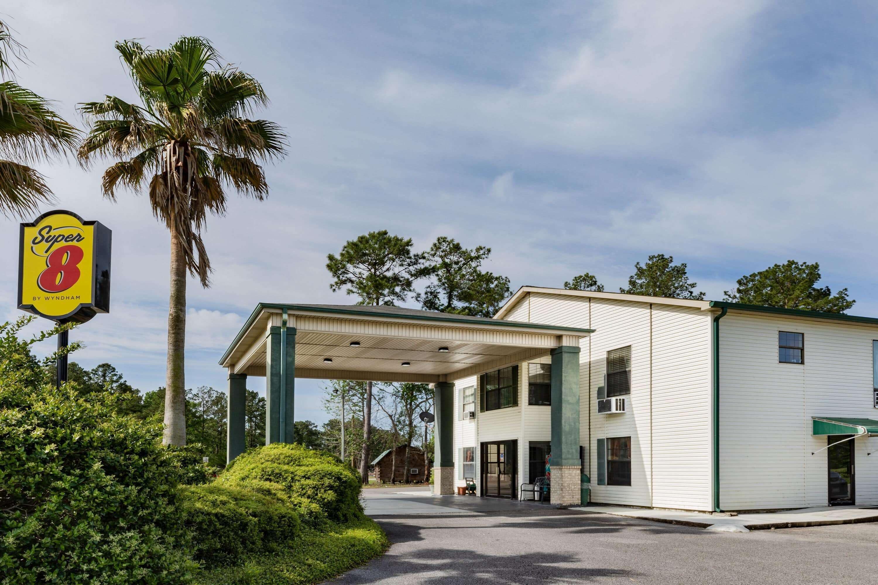 A Super 8 motel with a covered parking area, palm trees, and a clear sky.