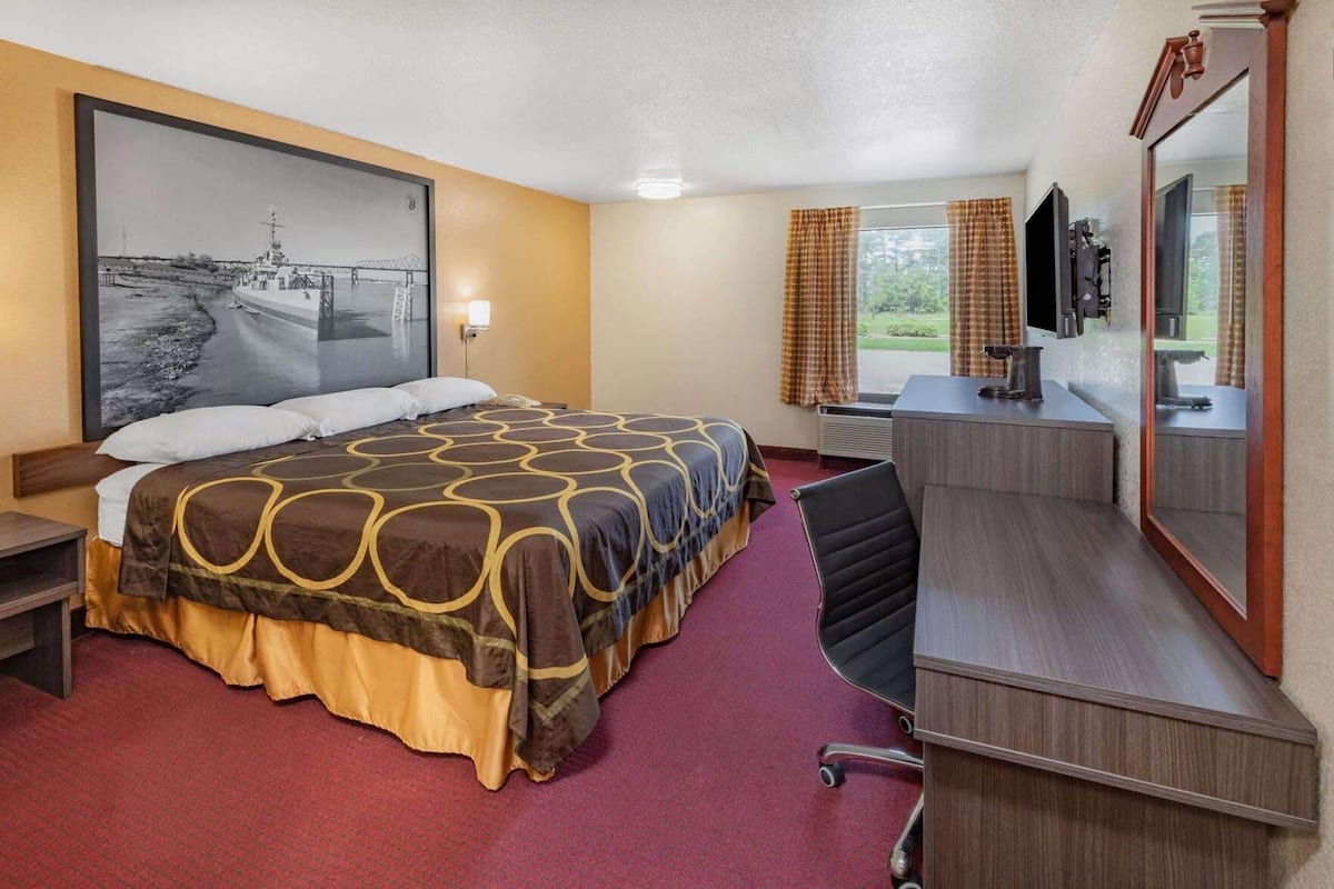Une chambre d’hôtel avec un grand lit, un bureau, une chaise, une télévision et une fenêtre avec des rideaux.