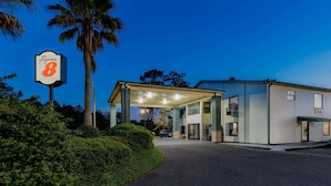 A Super 8 motel with a covered parking area, palm trees, and a clear sky. - Super 8 by Wyndham Kinder/Coushatta near Casino (Kinder)
