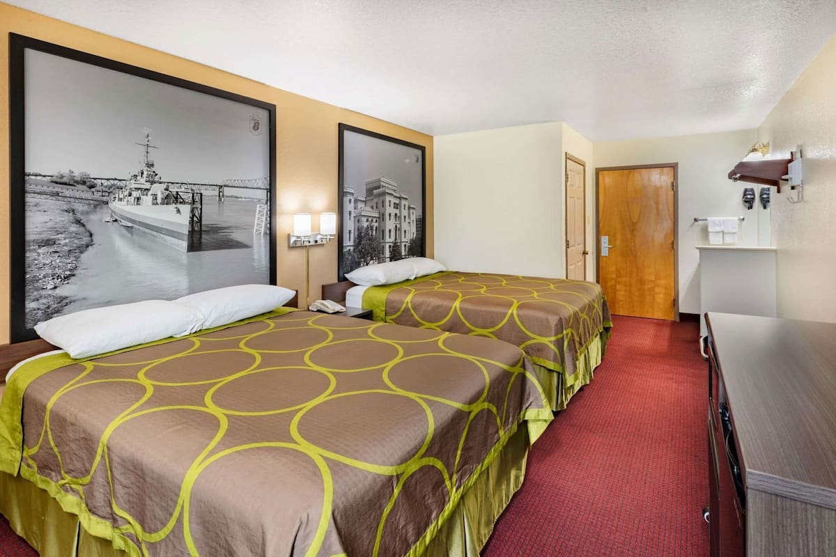 Une chambre d’hôtel avec deux lits, une moquette rouge, une porte en bois et un téléviseur fixé au mur.