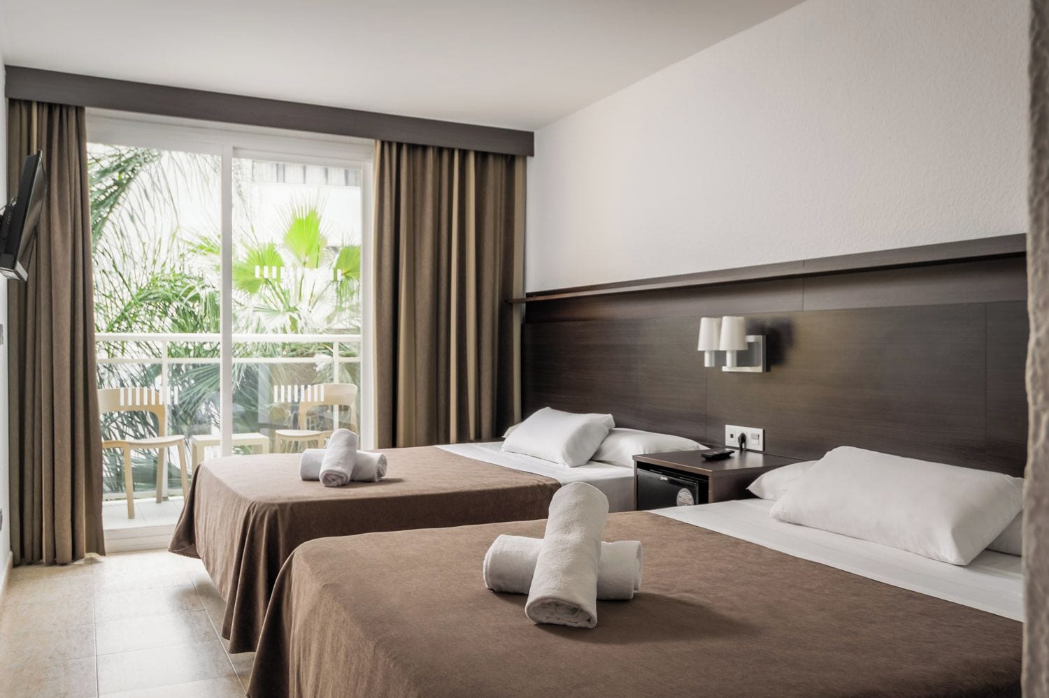 Habitación de hotel con dos camas, un balcón y vistas a zonas verdes.