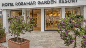 Hotel Rosamar Garden Resort con una entrada moderna, amplias puertas de cristal y plantas en macetas con flores moradas.