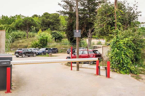 Un estacionamiento cerrado con varios coches aparcados, un coche rojo en primer plano y un cartel que indica prohibido el paso.