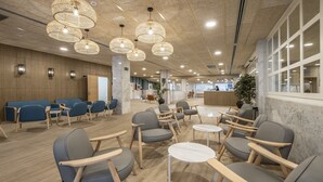 Un área de espera moderna con sillas azules y grises, mesas de madera y lámparas colgantes tejidas.