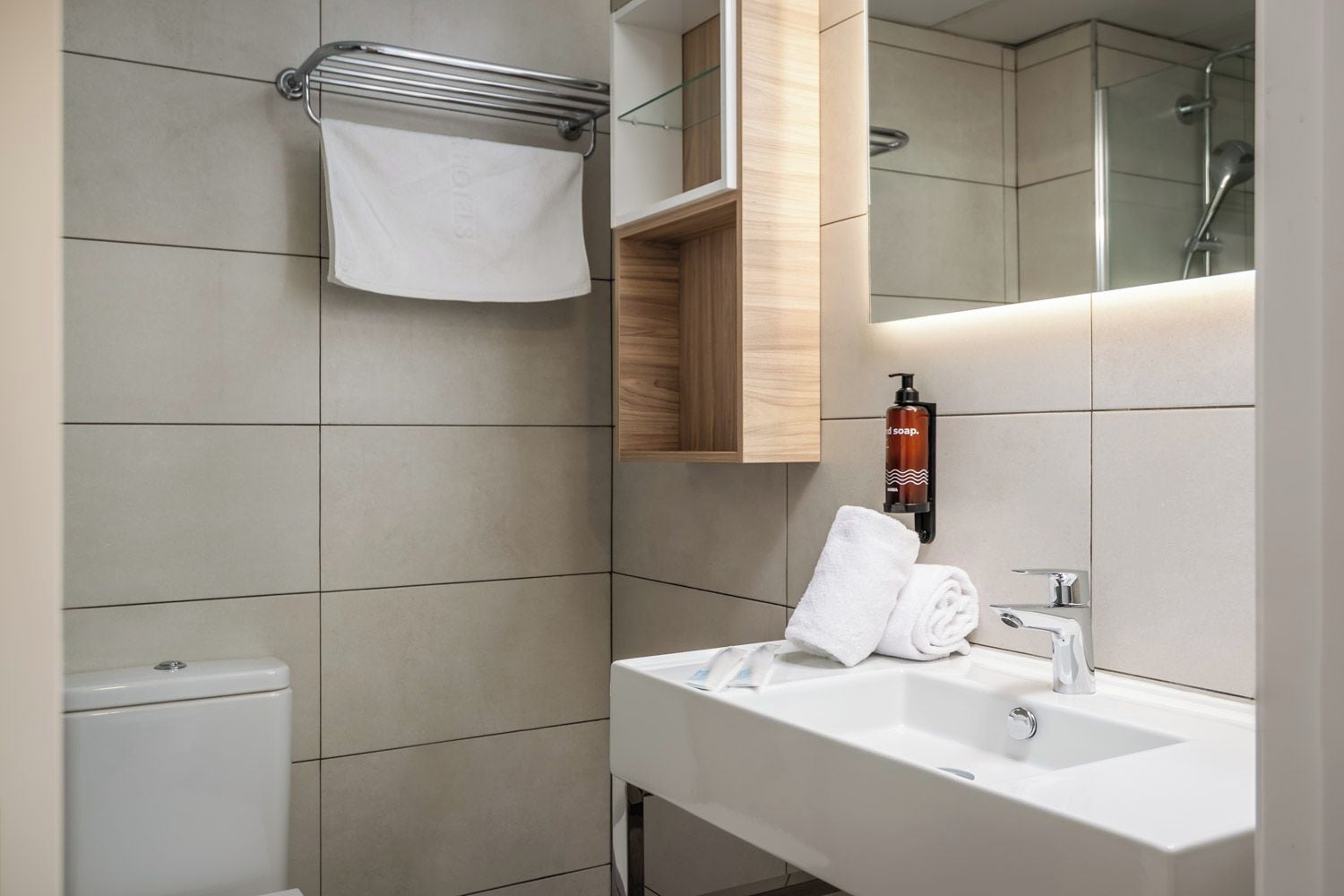 Un baño moderno con lavamanos blanco, espejo, toallero y zona de ducha.