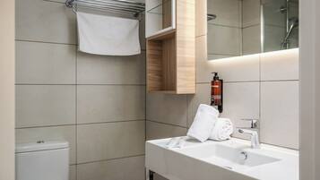 Un baño moderno con lavamanos blanco, espejo, toallero y zona de ducha.