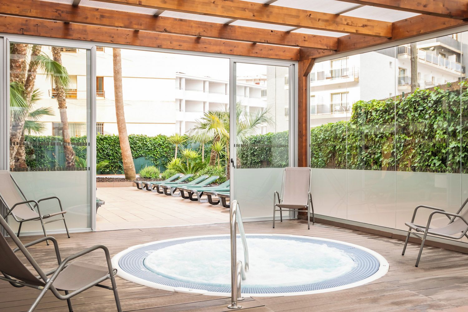 Un espace extérieur abrité comprenant un jacuzzi, des chaises longues et une vue sur un immeuble résidentiel et des espaces verts.