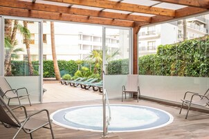 Un espacio al aire libre techado con un jacuzzi, sillones de descanso y vistas a un edificio residencial y follaje.