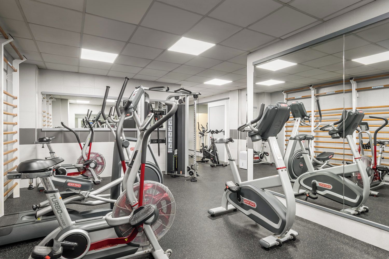 A gym with multiple cardio machines, weightlifting equipment, and mirrors on the walls.