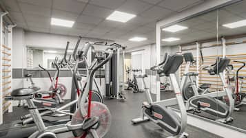 A gym with multiple cardio machines, weightlifting equipment, and mirrors on the walls.
