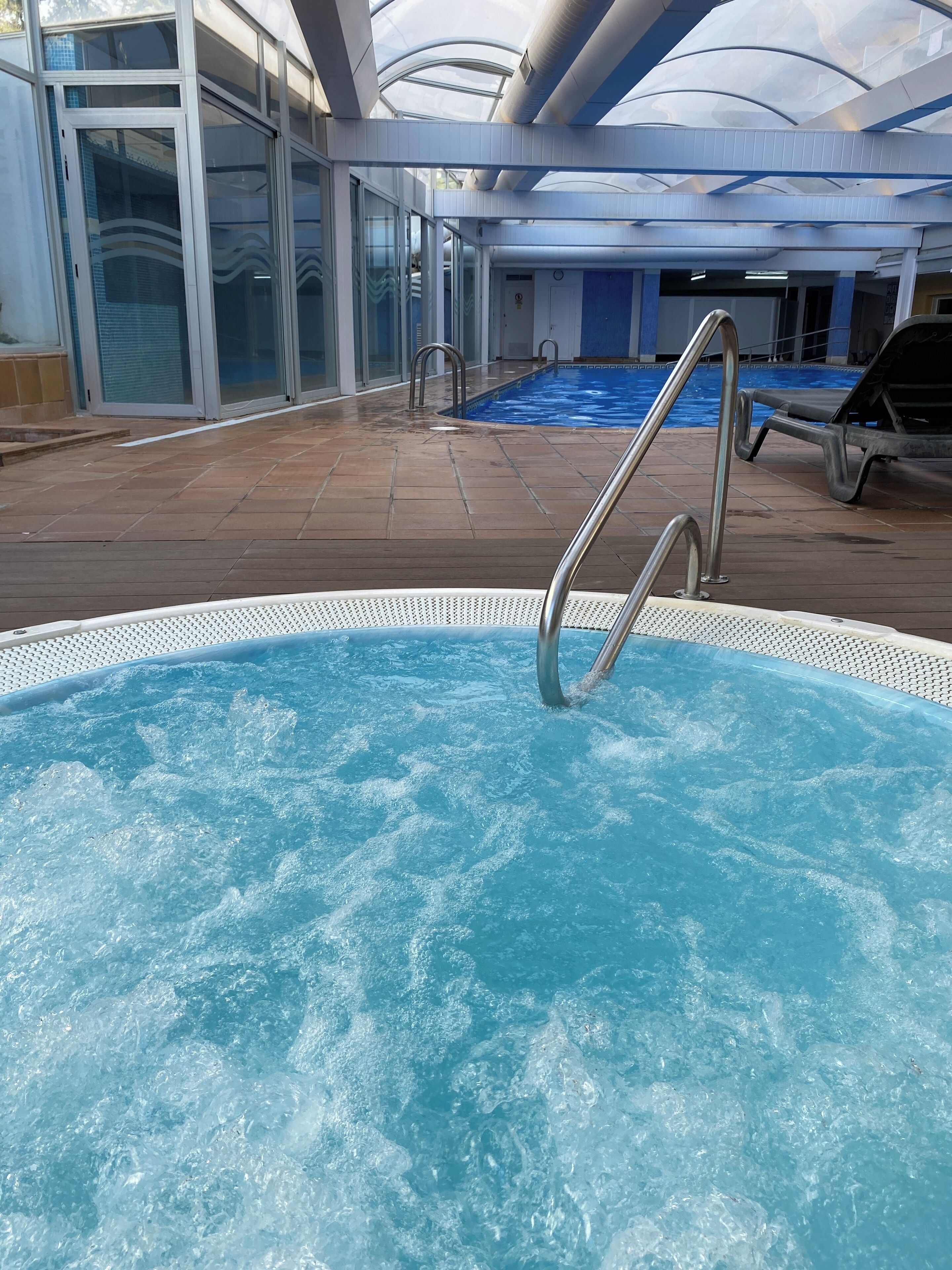 An indoor swimming pool with clear water, a metal ladder, and a tiled deck area.