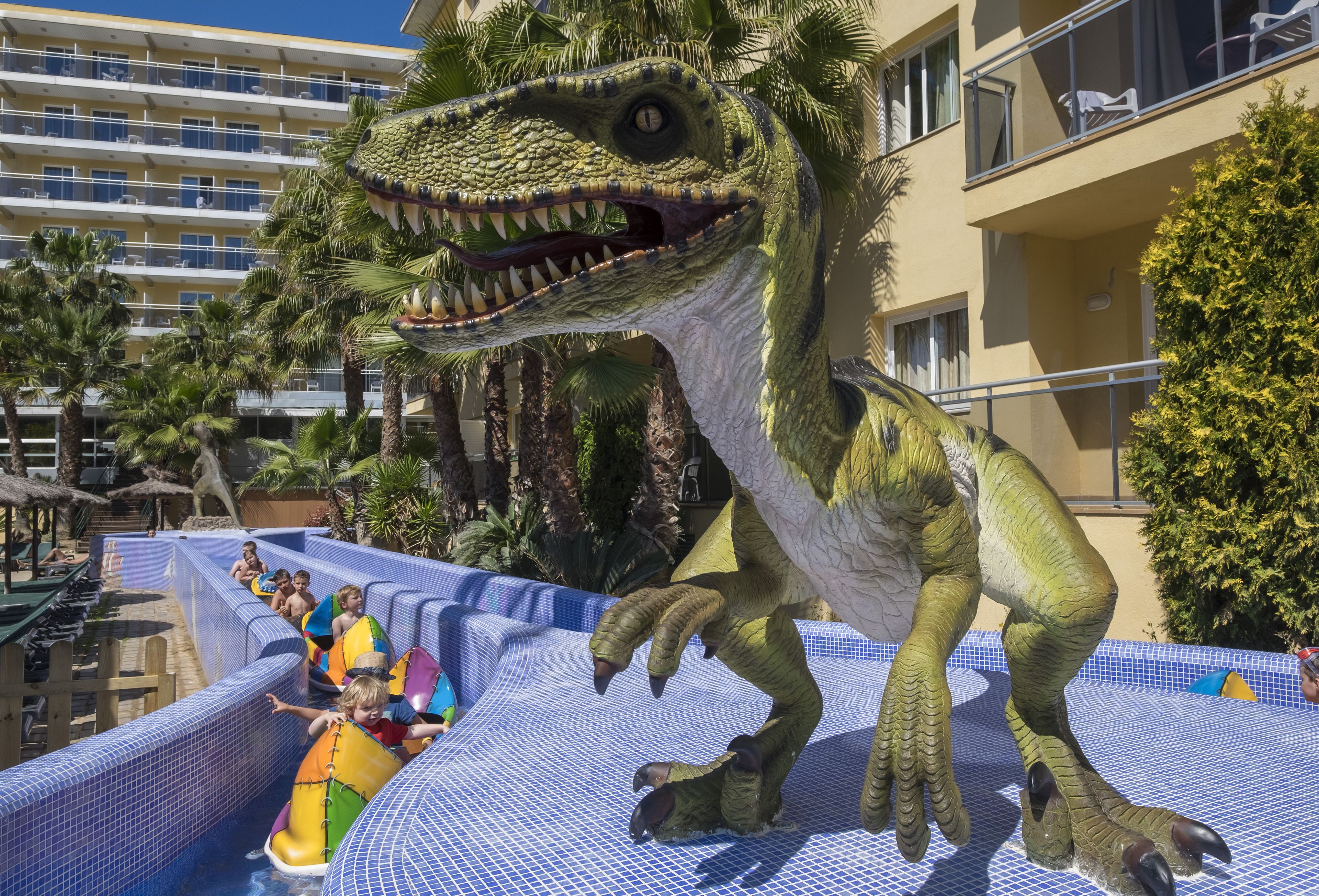A large inflatable dinosaur in a water park area with a pool and lounge chairs.
