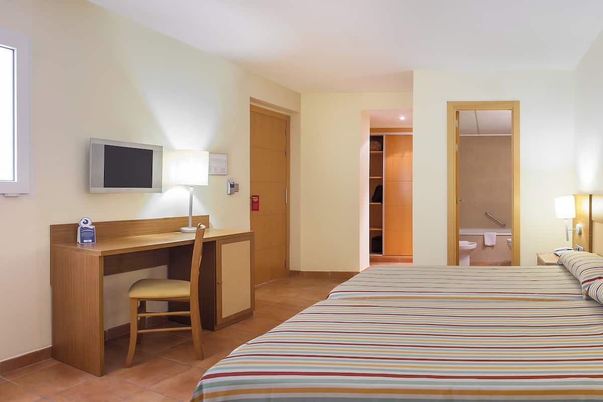 A hotel room with a bed, a desk, a chair, a TV, and a bathroom visible through an open door.
