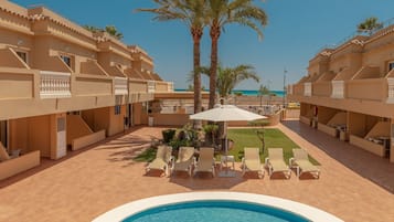 Zona de piscina en un resort con piscina central, tumbonas, palmeras y vistas a la playa.