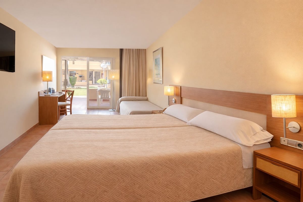 Ein Hotelzimmer mit zwei Betten, einem Schreibtisch und einem Stuhl. Es gibt einen Blick auf den Balkon.