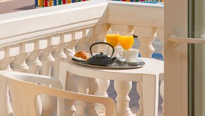 Un balcon avec une table dressée pour le petit-déjeuner, donnant sur une plage bordée de palmiers et offrant une vue lointaine sur une structure ressemblant à un château.