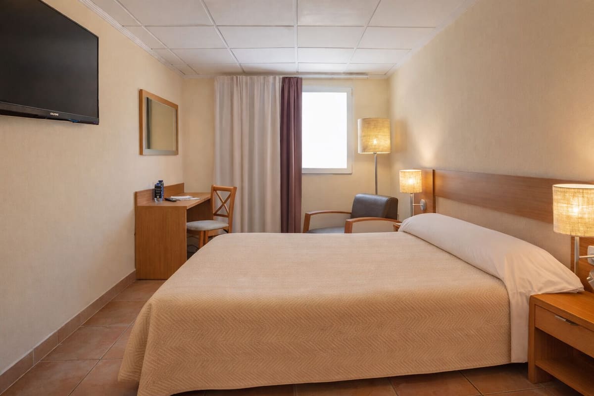 Ein Hotelzimmer mit Bett, Schreibtisch, Stuhl, Fernseher und zwei Lampen.