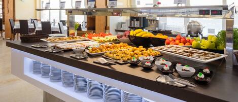 A buffet with various food items, including fruits, pastries, and desserts, arranged on a counter with plates and serving utensils.