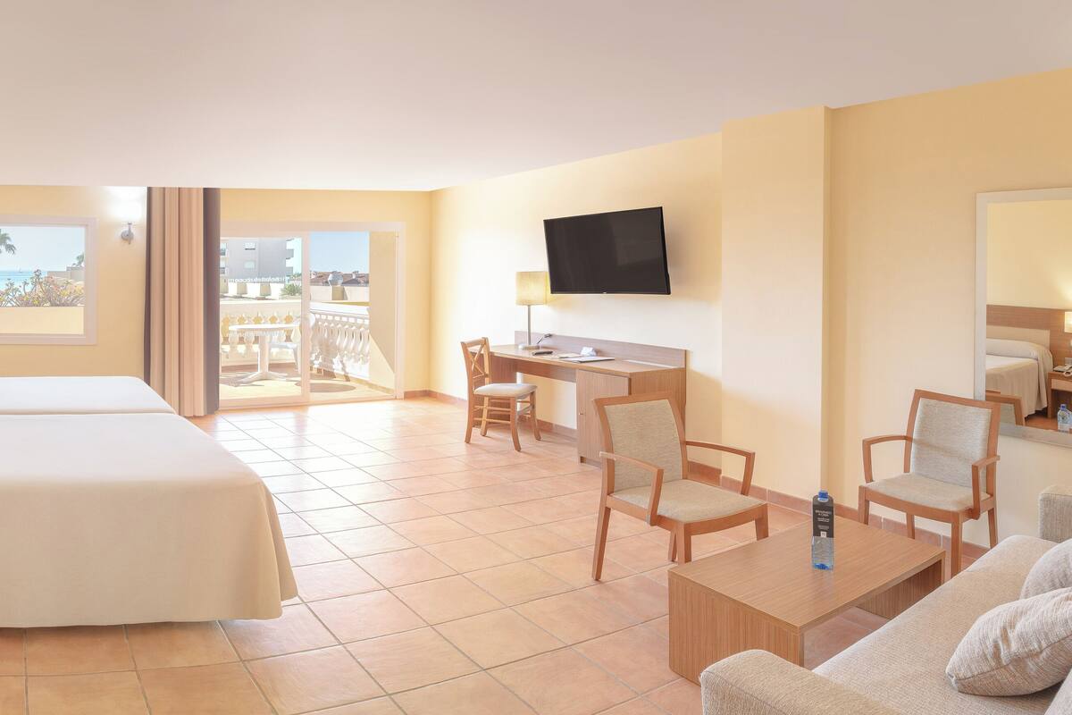 Ein Hotelzimmer mit zwei Betten, einem Schreibtisch, einem Sessel, einer Couch, einem Fernseher und einem Balkon mit Blick.