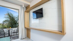 Un balcone con una TV a muro, un tavolo con sedie e vista su palme.