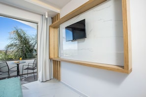 A balcony with a TV mounted on the wall, a table with chairs, and a view of palm trees.
